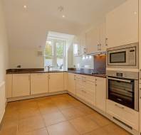 A modern kitchen with white cabinetry, dark countertops, a tiled floor, and a built-in oven and microwave.