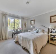 A bedroom with a queen-sized bed, two bedside tables with lamps, and a dressing table placed in front of a window.