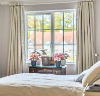 A bedroom with a bed in the foreground and a wooden desk beneath a window, holding potted plants and a framed photo.