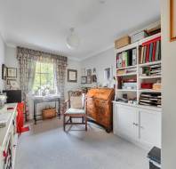 A home office with a desk, a wooden writing bureau, a chair, and a large white shelving unit filled with books and folders.