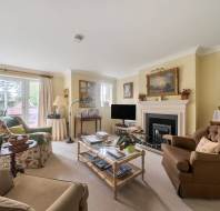 A living room featuring a fireplace, a flat-screen TV, a glass-topped coffee table, and several upholstered armchairs.