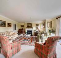 A living room with two plaid armchairs, a striped sofa, a green sofa, and a fireplace, with several paintings hanging on the walls.