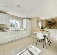 Modern kitchen with white cabinets, a square dining table with four chairs, and a landscape painting on the wall.