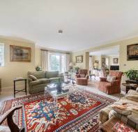 A living room with a large patterned rug, a green sofa, two plaid armchairs, and a glass coffee table.