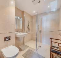 A beige-tiled bathroom featuring a wall-mounted toilet, a pedestal sink, and a glass-enclosed walk-in shower.