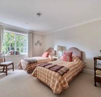Bedroom with two twin beds featuring tan and white plaid bedspreads, a wooden chair, and a tiered side table.