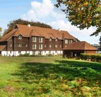 Large brown building with a tiled roof and white ground floor, situated next to a grassy field.