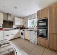Modern kitchen featuring white and light wood cabinetry, built-in wall ovens, and laundry appliances integrated under the counter.