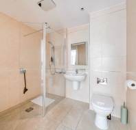Bathroom with beige tiles, a glass-enclosed walk-in shower, pedestal sink with a mirror, and a toilet next to a towel radiator.