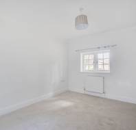 An empty room with white walls, carpeted flooring, a window, a radiator, and a ceiling light.