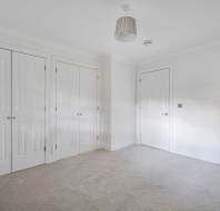 An empty room with beige carpet, white walls, two sets of double closet doors, and one single door.