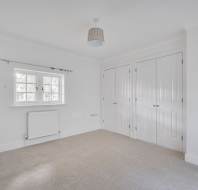 Empty white room with beige carpet, a single window with a radiator below it, and double white closet doors.