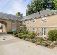 Two-story tan brick building with a stone-paved driveway, a large arched entryway, and a small garden patio.
