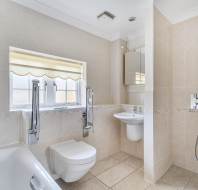 A tiled bathroom featuring a wall-mounted toilet, a pedestal sink, a bathtub with a handheld shower faucet, and a walk-in shower area with a wall-mounted shower head.