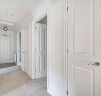 A hallway with light carpeting and several closed white doors.