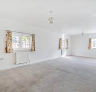 Empty, white-walled room with beige carpet, three windows with floral curtains, and two pendant lights.
