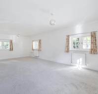 An empty room with white walls, beige carpet, and three windows with patterned curtains.