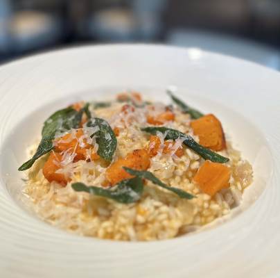A plate of risotto topped with chunks of roasted pumpkin, sage leaves, and grated cheese.