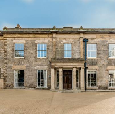 A large, two-story stone building with symmetrical windows and a central entrance featuring columns, set against a clear sky.