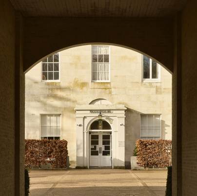 An arched brick passageway frames a view of a white building facade. The entrance has a white door with rectangular windows on either side and "Scott Polar Institute" above it.