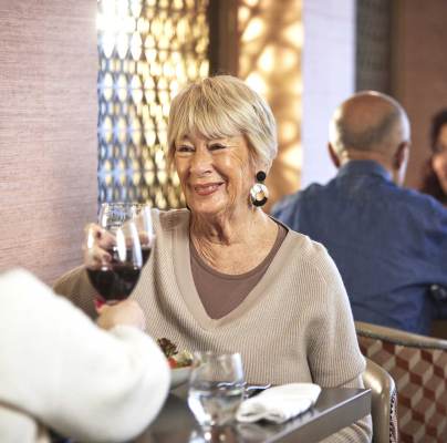 Two older adults enjoying drinks and conversation at a restaurant, with another couple seated in the background.