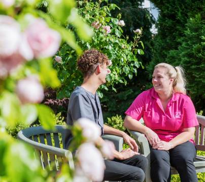 Man and woman in carer's uniform, sitting in rose garden