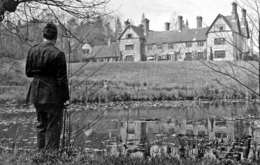 A black and white old picture of a soldier's back looking to a manor house