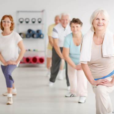 Low impact fitness class with seniors bending a knee and leaning forward