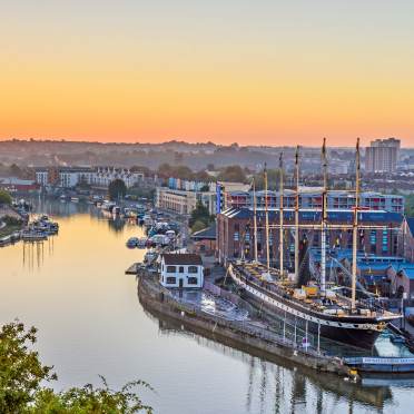 Waterfront at sunset with tall-masted ship