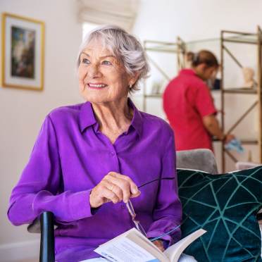 Elderly woman reading while carer cleans