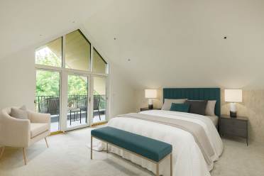 A modern bedroom with a large window and balcony. It includes a bed with a teal headboard, two nightstands with lamps, a beige armchair, and a teal bench at the foot of the bed.