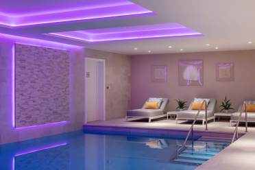 Indoor pool area with a seating section. Purple LED lights illuminate the ceiling. Two lounge chairs with cushions and small plants are against a textured wall.