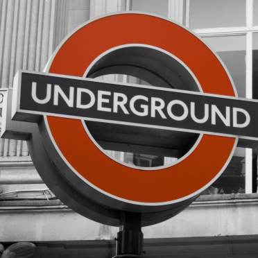 A red and white London Underground sign is displayed outside a building with columns and windows in the background.