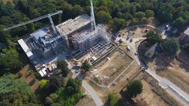 Cooper's Hill House and The Chapel Aerial view of a construction site with cranes, a partially built structure, vehicles, and surrounding trees and roads.