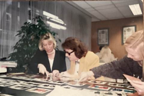 Three people examining photographs spread across a table in an office setting.