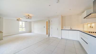 Spacious, unfurnished open-plan living room and kitchen with white walls and tile flooring, featuring large window and modern light fixtures.