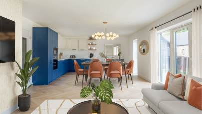 Modern living room and kitchen area with a blue and white kitchen, orange chairs, and a round chandelier. A sofa, coffee table, and plant are in the foreground near large windows.