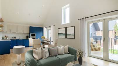 Modern living room with a green sofa, decorative pillows, and coffee table. Adjacent kitchen area with blue and white cabinetry. Large windows and a balcony door provide natural light.
