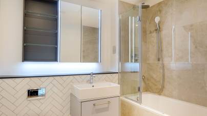 Modern bathroom with a wall-mounted sink, illuminated mirror, tiled walls, bathtub, and glass shower screen.