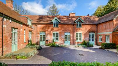 A red-brick house with green doors and windows, surrounded by a landscaped courtyard and greenery.