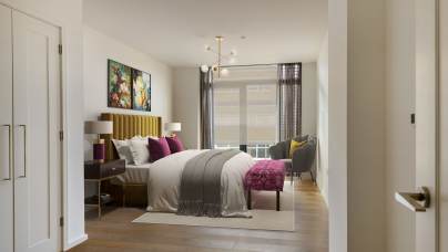 A modern bedroom with a bed, decorative pillows, artwork on the wall, two nightstands with lamps, a chair by the window, and wood flooring. A chandelier hangs from the ceiling.