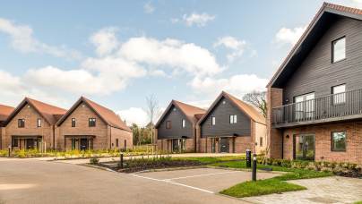 Row of modern, two-story houses with pitched roofs and brick walls, set against a blue sky with scattered clouds.
