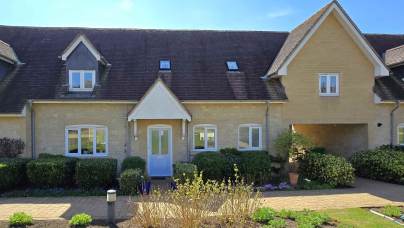Front view of a two-story house with a pitched roof, dormer windows, a blue front door, and a landscaped garden under a clear blue sky.