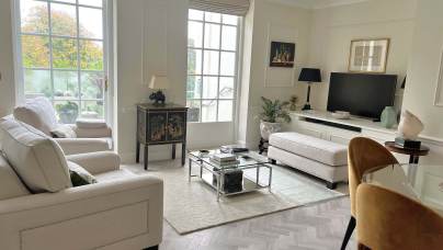 Bright, modern living room with large windows, neutral furniture, a TV on a console, glass coffee table, and art on the walls.