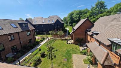 A sunny courtyard surrounded by modern brick residential buildings, with green grass, small trees, and paved walkways.