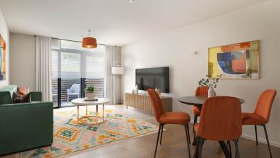 A modern living and dining area features a green sofa, orange chairs, a patterned rug, a TV on a wooden stand, and large windows with sheer curtains.