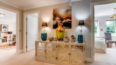 A hallway with a decorative sideboard, vases, lamps, and artwork, leading to a living room on the left and a bedroom on the right with large windows.