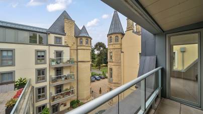 View from a modern balcony overlooking neighboring apartments with balconies and a historic building featuring two pointed towers, under a partly cloudy sky.