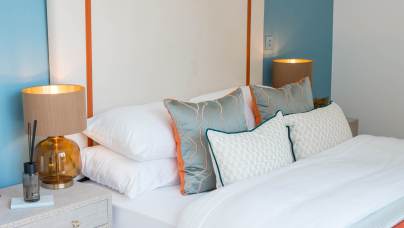 Modern bedroom with a bed made up in white linens, decorative pillows, and two bedside tables holding matching lamps with beige shades and amber glass bases.