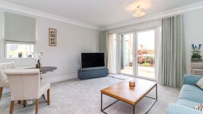 Bright living room with light carpeting, a sofa, coffee table, TV, small dining table with chairs, and glass doors leading to a patio.
